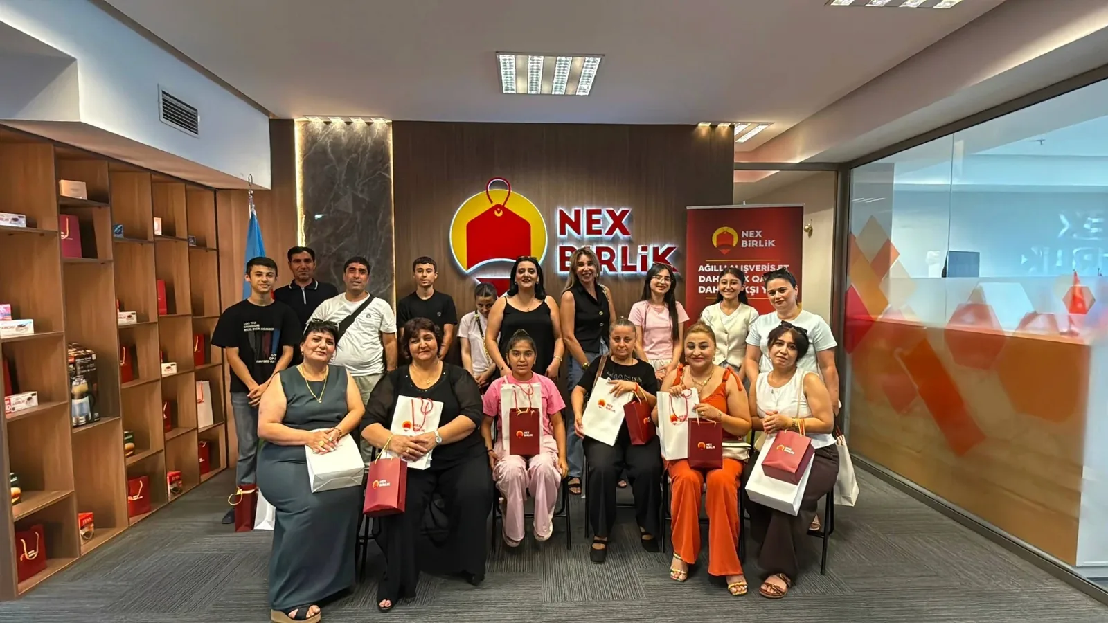 NexBirlik ofisinde marka panosu önünde topluluk grup fotoğrafı